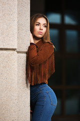 Sad young fashion woman in leather jacket on city street