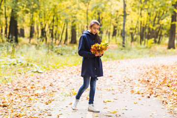 Young beautiful happy teen girl woman holding bouquet of autumn leaves and smiling, on background of forest