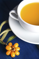 Obraz na płótnie Canvas ripe sea buckthorn berries next to a white ceramic cup with tea from the berries on the table