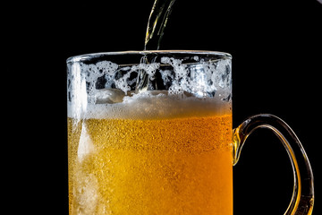 Stream of beer being pouring into a glass with beer and foam closeup, splashing, splash
