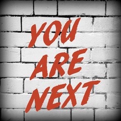 The words You Are Next in red text on a white brick wall background as a warning or a reminder