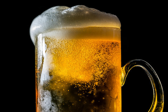 Beer overflowing large glass with foam and bubbles isolated on a black background