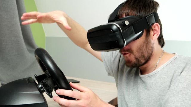 crazy guy wore glasses for virtual reality and plays with a car wheel. Young man wearing virtual reality Glasses. His living room transforms into space - with special visual effects