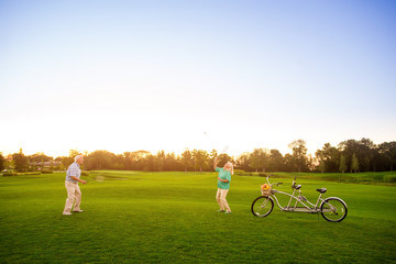 Senior couple playing badminton. Bicycle on the lawn. Lightness of movements. Do sports and be healthy.