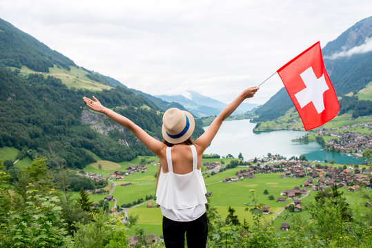 Young woman with swiss flag enjoying great landscape view on the valley with lake and village in Switzerland.