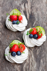 Mini  Pavlova meringue cakes with berries and lime on rustic woo
