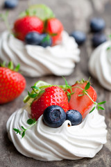 Mini  Pavlova meringue cakes with berries and lime on rustic woo