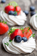 Mini  Pavlova meringue cakes with berries and lime on rustic woo