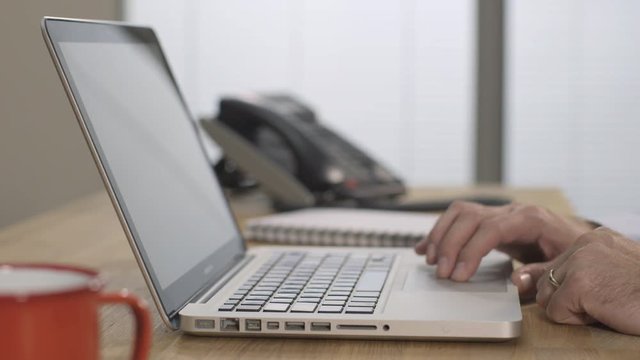 Male hands typing and using the trackpad on a silver laptop computer.