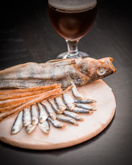 Glass of beer and assorted dried fish on a cooking sheet, traditional beer snack. Black wooden background.