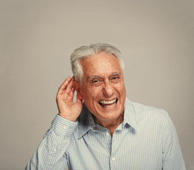 Deaf senior man holding hand near ear.