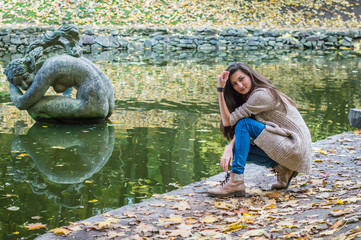 beauty girl sitting near the pond in the autumn park