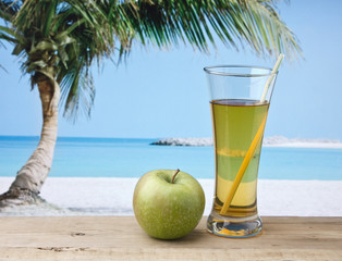 Glass of apple juice on a beach table