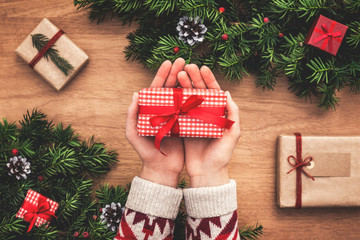 Female holding red checked christmas gift with red ribbon onchristmas tree background.