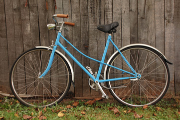 Fototapeta na wymiar Classic vintage retro city bicycle in blue leaning against wood texture fence.