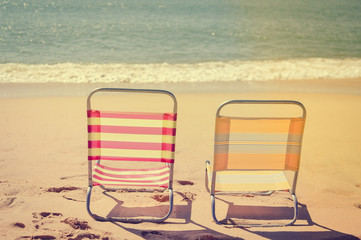 Back view of two beach chairs on sandy beach sunny outdoors background.