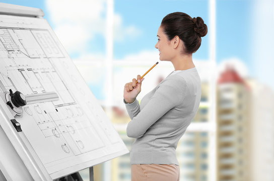 Young female engineer working with project on drawing board in office