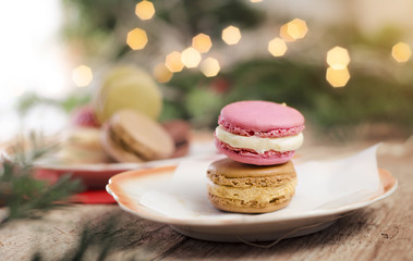 Delicious sweets on plate, macaroons on natural wooden texture and Christmas lights in background