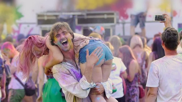 Young drunk man holding sexy woman on shoulders, dancing at Holi fest, crazy fun