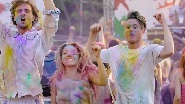 Happy people moving to music at Holi festival, friends covered in colored paint