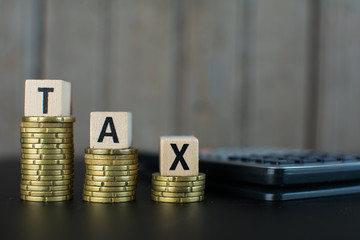 Tax Concept with wooden block on stacked coins and a calculator on the background