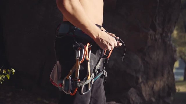Side view of unrecognizable topless climber rubbing his hands with chalk in sunlight