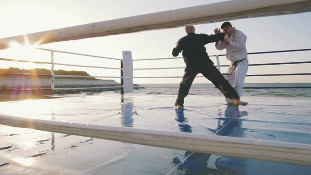 Two professional karate fighters are fighting on the beach boxing ring, slowmo