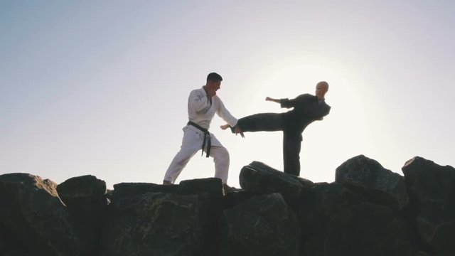 Two male karate fighters posing on stones sea background, slow motion