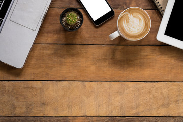 Office desk table with laptop, blank screen smartphone, blank screen tablet, leather notebook and cup of coffee.Top view with copy space.Office supplies and gadgets concept.