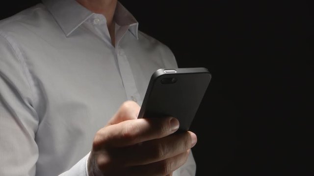 Man in white shirt holds a smartphone by hand and touches on it (half-side)