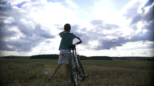 Boy with bike standing in a field at the top and looking, than going