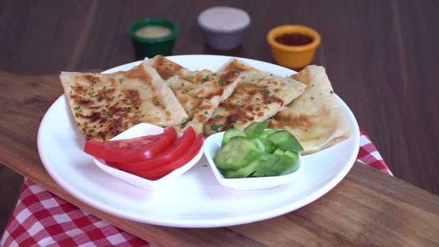 Turkish traditional Gozleme pita potatoes with cucumber and sliced tomato rotating on scotch pattern fabric