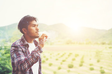 Fototapeta premium Hipster man smoking cigarette, standing behind a mountain. Among
