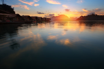 Obraz premium Silhouette scenery during sunrise of houseboat resort at lake river in natural attractions,Ratchaprapha Dam at Khao Sok National Park,Surat Thani Province in Thailand.Traveling , recreation Concept