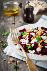 Salad of beetroot, feta and walnuts with leaves of parsley on the old wooden background. Selective focus.