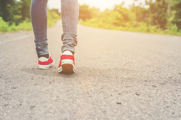 Woman feet with red sneaker shoes walking on the roadside.