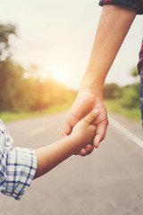 Mother holding hand of her son outdoors in summer walking on the