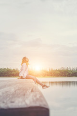 Young beautiful hipster woman sitting on the lake relaxing with