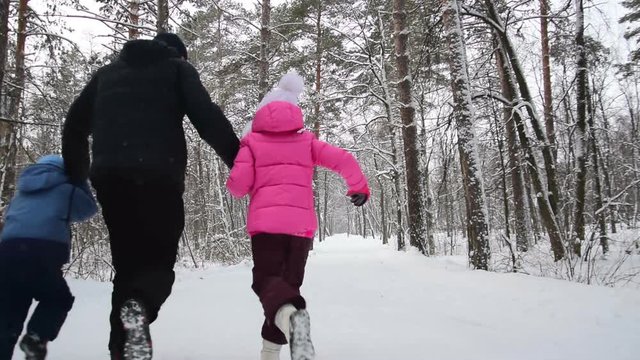 Man and two his children hold hands and run in the winter forest. Slow motion
