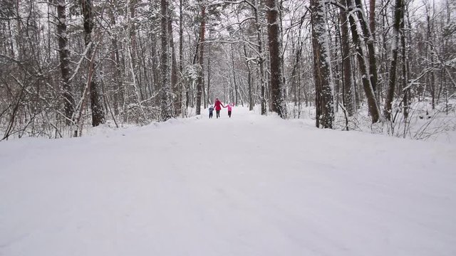 Woman and two his children hold hands and run in the winter forest. Slow motion
