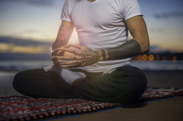 Cropped shot of man practicing yoga on the beach at sunset. Man sitting in lotus position and meditating