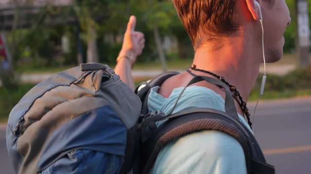 Young Tourist with Backpack Hitchhiking along a Road in Sunset