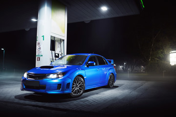 Fototapeta na wymiar Blue car stay on gas fuel station in city at night