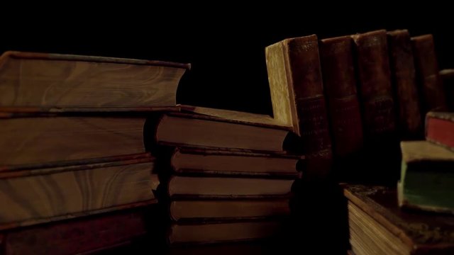 Old, aged books in a row on a wooden table. Camera panning and moving.
