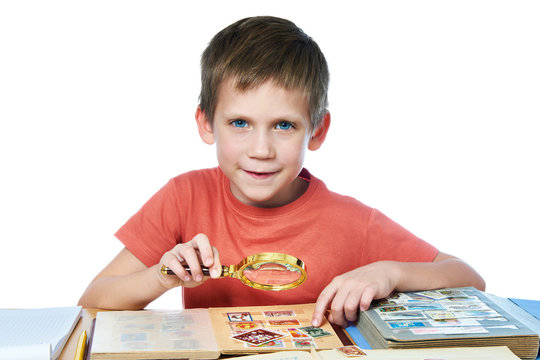 Boy with magnifier looks his stamp collection isolated