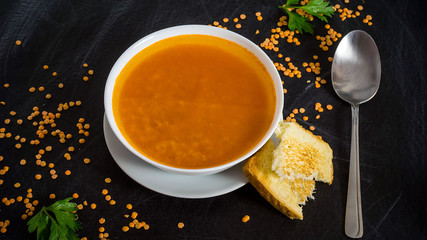 Delicious red soup on dark background, toasts, lentil. Top view