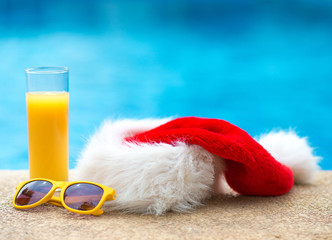 Obraz na płótnie Canvas Christmas hat, sunglasses and orange juice near the pool.