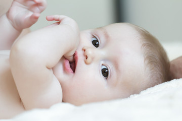 Close up portrait of infant sucking thumb and lying on white bed