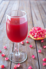 Close up of a glass of pomegranate juice with fresh pomegranate on a wooden table.