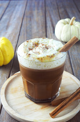 Close up of a glass of pumpkin spice latte with whipped cream on a wooden plate.